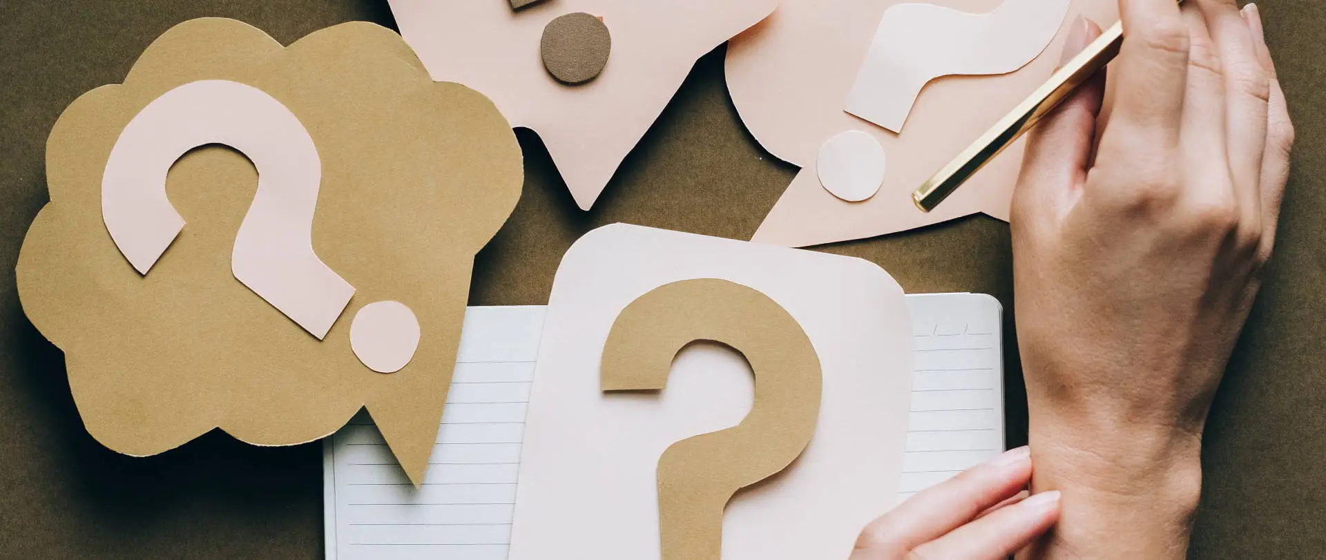 content in Q&A format Hands placing a large white question mark on a desk next to a speech bubble icon, symbolizing question-and-answer content strategy.